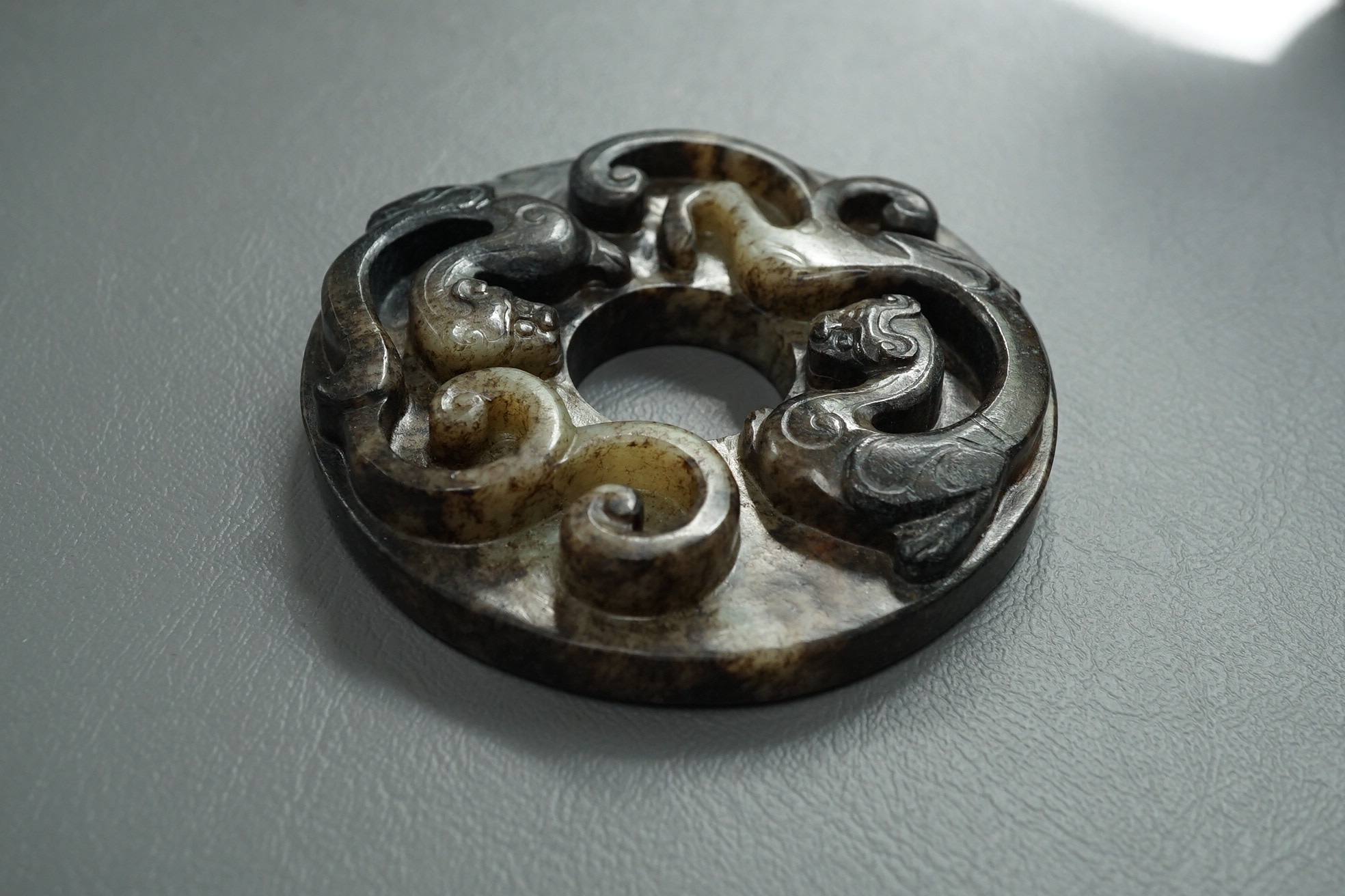 A Chinese pale celadon and black jade bi disc